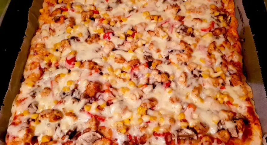 Pyszny przepis na pizzę z kurczakiem, kukurydzą i pieczarkami, obficie posypaną ciągnącym się serem.