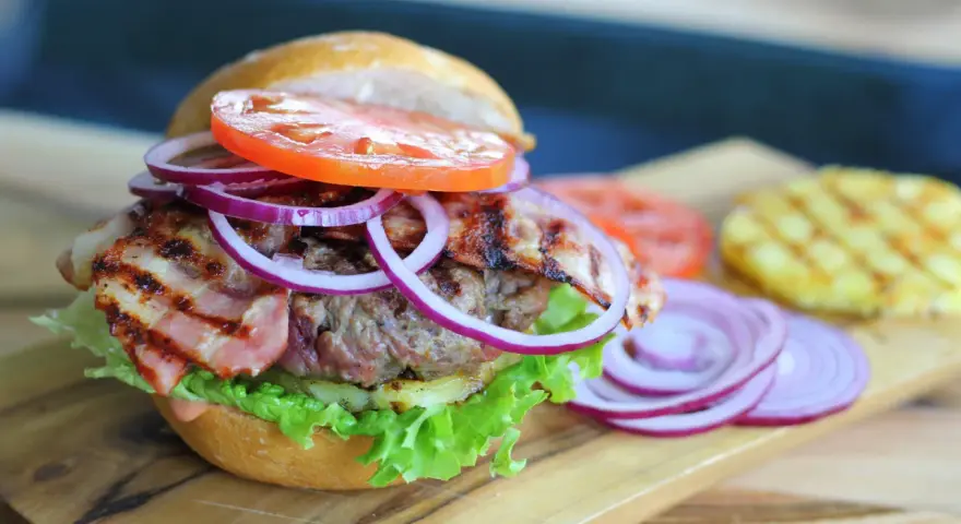 Soczysty burger z chrupiącym boczkiem, pomidorem, sałatą i czerwoną cebulą. Dodatki do burgera kuszą smakiem.
