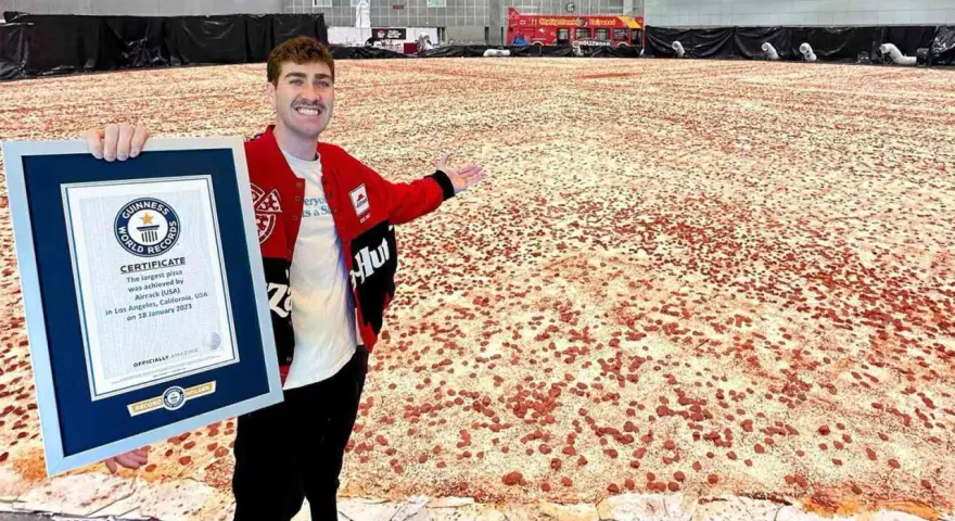 Mężczyzna prezentuje certyfikat Guinnessa za największą pizzę świata, która rozciąga się na ogromnej przestrzeni.