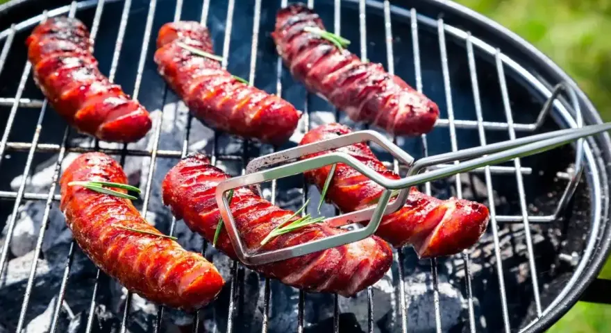 Aromatyczna kiełbasa z grilla, skwiercząca na węglu, z gałązkami rozmarynu. Idealna na letnie popołudnie.