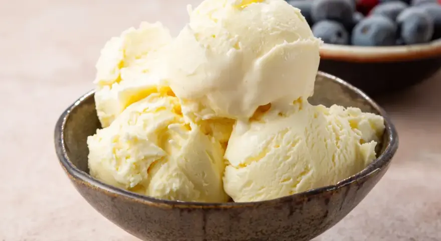 Pyszne, kremowe domowe lody waniliowe w miseczce, obok miseczka z jagodami i malinami.