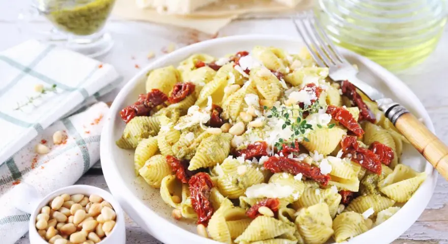 Pyszny makaron z pesto i suszonymi pomidorami, posypany parmezanem i orzeszkami pinii.