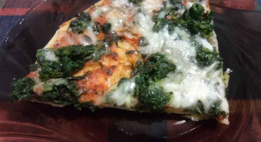 Kawałek pysznej pizzy ze szpinakiem, z ciągnącym się serem i pomidorowym sosem, na ciemnym talerzu.