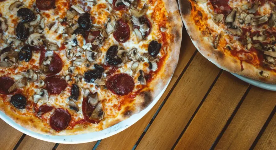 Dwie pizze z bogactwem składników na wierzchu: salami, pieczarki i czarne oliwki. Idealne na wspólny posiłek.