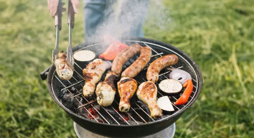 Pyszne kiełbaski i kurczak pieką się na grillu, a dym unosi się w powietrzu. Idealny sposób, jak rozpalić grilla i cieszyć się latem.