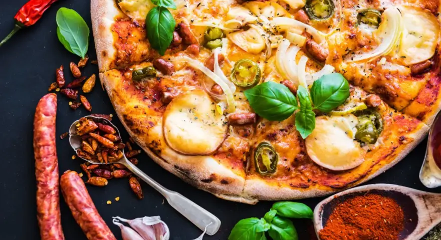 Apetyczna pizza z kiełbasą, cebulą i papryczkami jalapeño, otoczona składnikami.