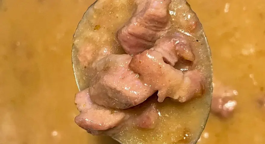 Łyżka pełna aromatycznego sosu z karkówki, z kawałkami mięsa w kremowym sosie.