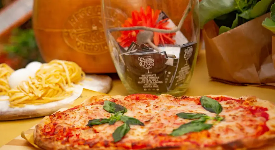Pyszne rodzaje pizzy, makaron i ser parmezan. W tle szklany wazon z ozdobami i kwiatami.