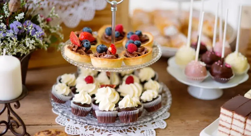 Słodkie przekąski: babeczki, tartaletki z owocami, cake pops i ciasto czekoladowe na drewnianym stole.