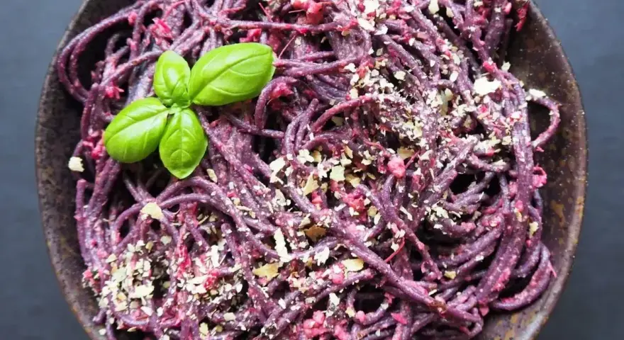 Fioletowy makaron z buraczanym pesto ze słoika, posypany orzechami i udekorowany listkiem bazylii.