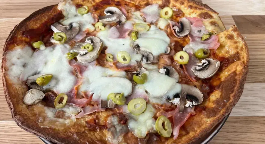 Apetyczna pizza z twarogu z pieczarkami, szynką i oliwkami, z ciągnącym się serem.