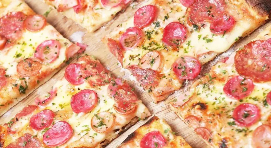 Kawałki pysznej pizzy cienkie ciasto z kiełbasą i serem, posypane ziołami. Idealna na szybką przekąskę.