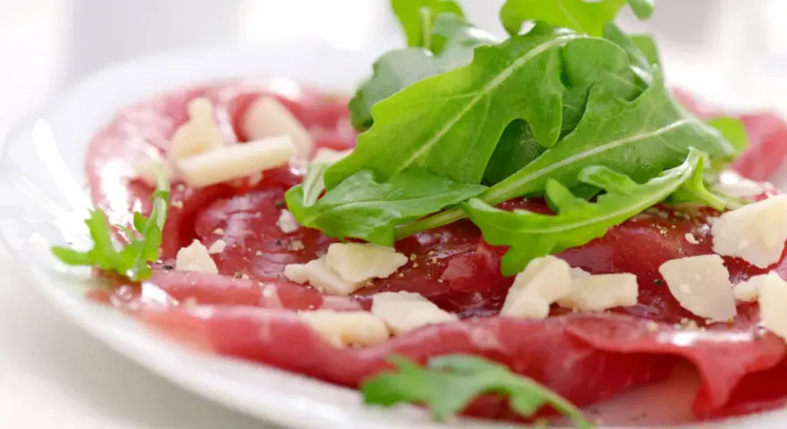 Cienkie plastry wołowiny z rukolą i parmezanem, polane pysznym sosem do carpaccio.
