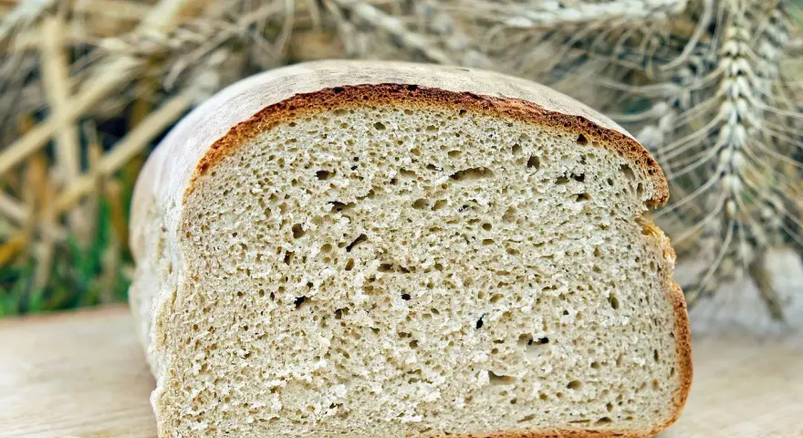 Świeży bochenek chleba na desce, idealny do rozmrożenia. W tle kłosy zbóż.