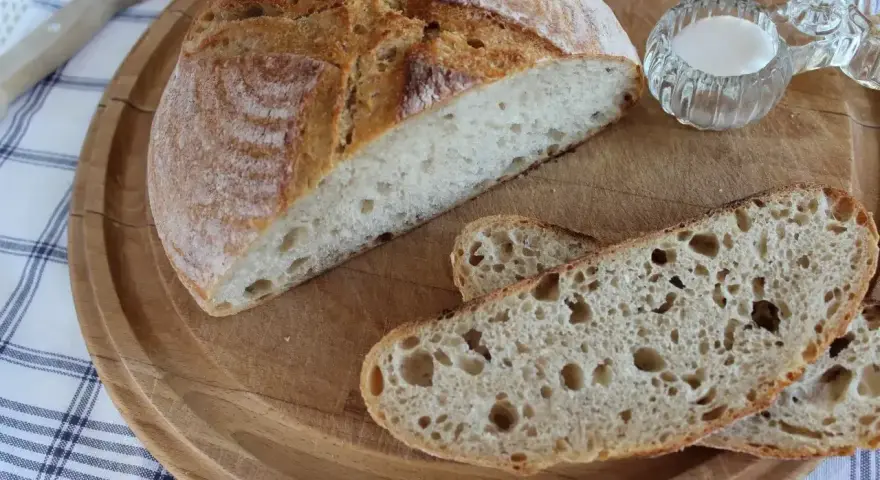 Chleb pszenno żytni na zakwasie, pokrojony na desce, z solniczką i nożem w tle.