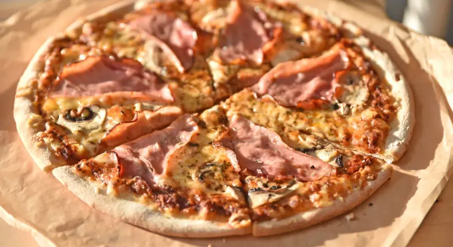 Pizza z szynką i pieczarkami, idealna na szybki obiad. Jakie pieczarki do pizzy? Te ciemne, pokrojone w plasterki, świetnie komponują się z serem i wędliną.