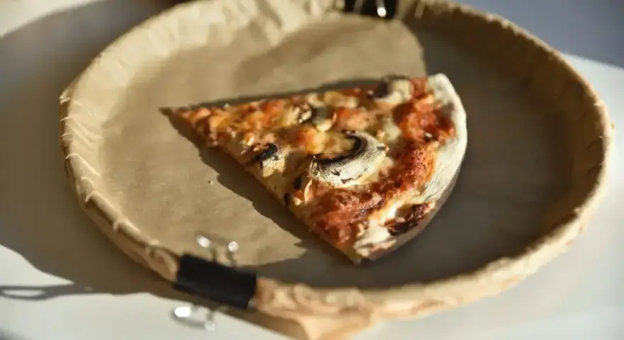 Kawałek pizzy z pieczarkami na brązowym papierze. Zastanawiasz się, ile kalorii ma pizza?