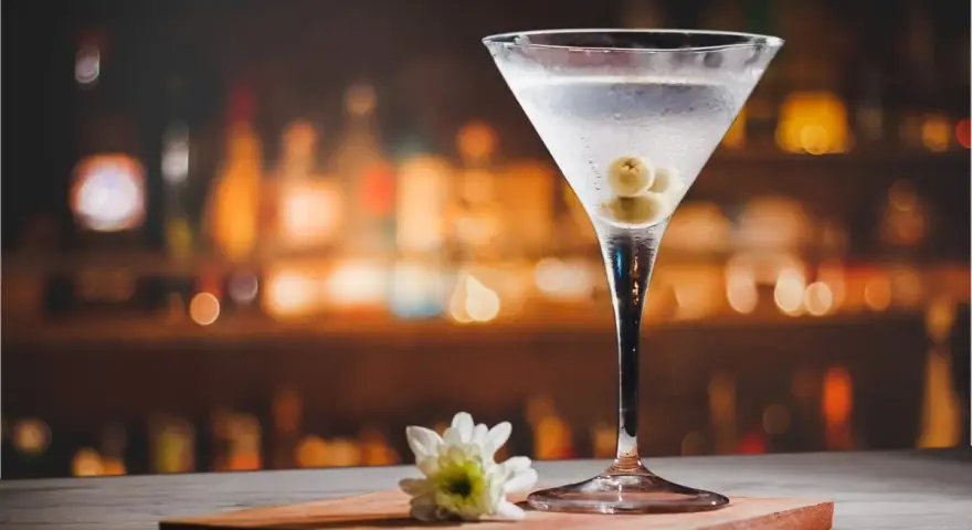 Kryształowy kieliszek z martini, trzema oliwkami i białą kwiatową ozdobą. Idealny drink, z czym pić martini?