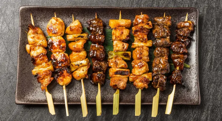 Różnorodne yakitori na talerzu: kurczak, warzywa i inne przysmaki, apetycznie wyglądające i gotowe do jedzenia.