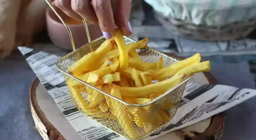Ręka sięga po chrupiące frytki z koszyka. Idealne do airfryera, by cieszyć się smakiem bez nadmiaru tłuszczu.
