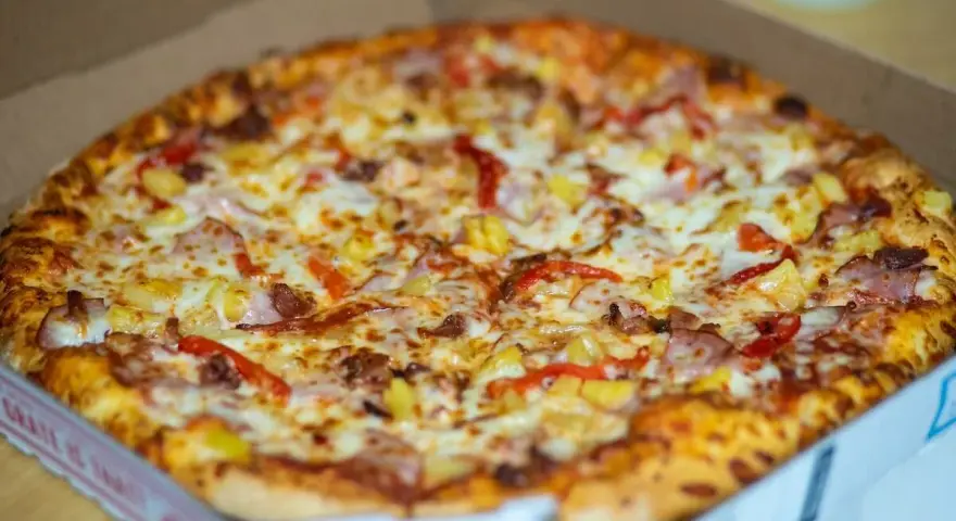 Pyszna, gorąca mrożona pizza w mikrofali, prosto z pudełka. Złocisty ser, kawałki ananasa i papryki kuszą apetycznie.