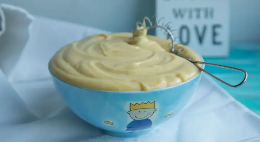 Gładki, kremowy krem patissiere w niebieskiej miseczce z małym królem. Idealny do deserów.
