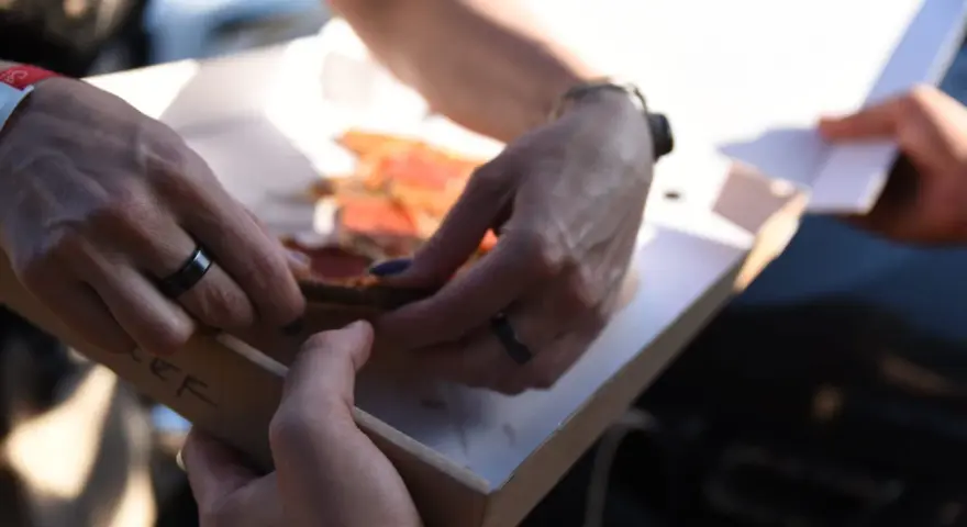 Dwie osoby dzielą się pizzą z pudełka. Właśnie pokazują sobie, jak jeść pizzę, by każdy dostał swój kawałek.