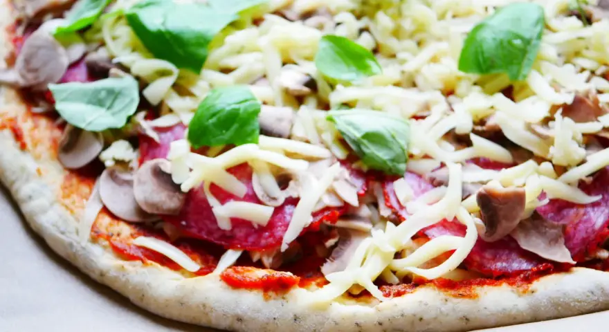 Gotowy do pieczenia przepis na ciasto do pizzy: sos pomidorowy, salami, pieczarki, ser i świeża bazylia.