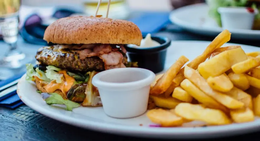 Pyszny burger z bekonem i frytki na talerzu. Idealny sposób, jak jeść burgera w restauracji, by delektować się każdym kęsem.