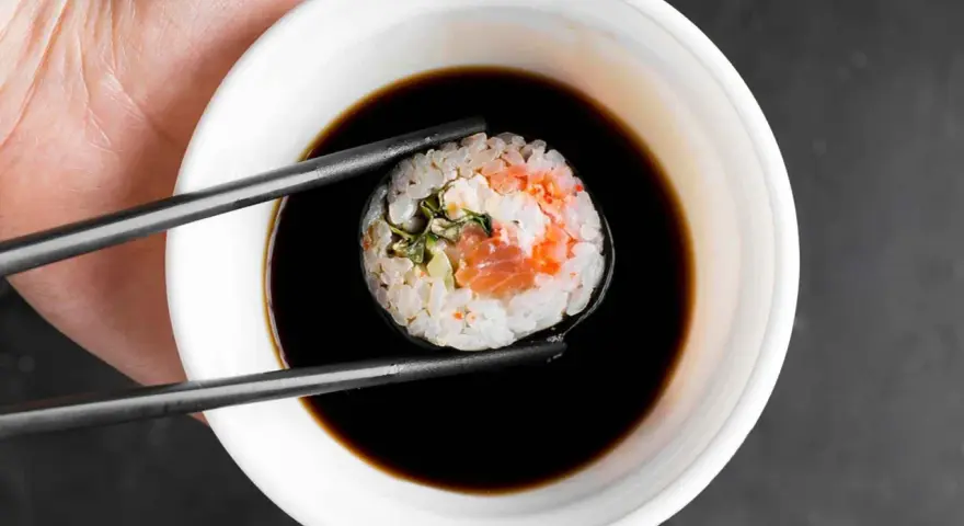 Pałeczki trzymają sushi z łososiem, zanurzając je w ciemnym sosie do sushi.