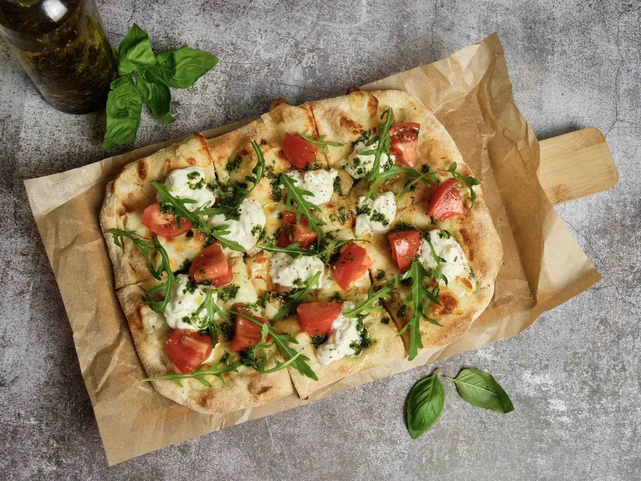 Pyszna pizza bez mięsa z pomidorami, mozzarellą i rukolą, polana zielonym pesto. Idealna dla wegetarian.