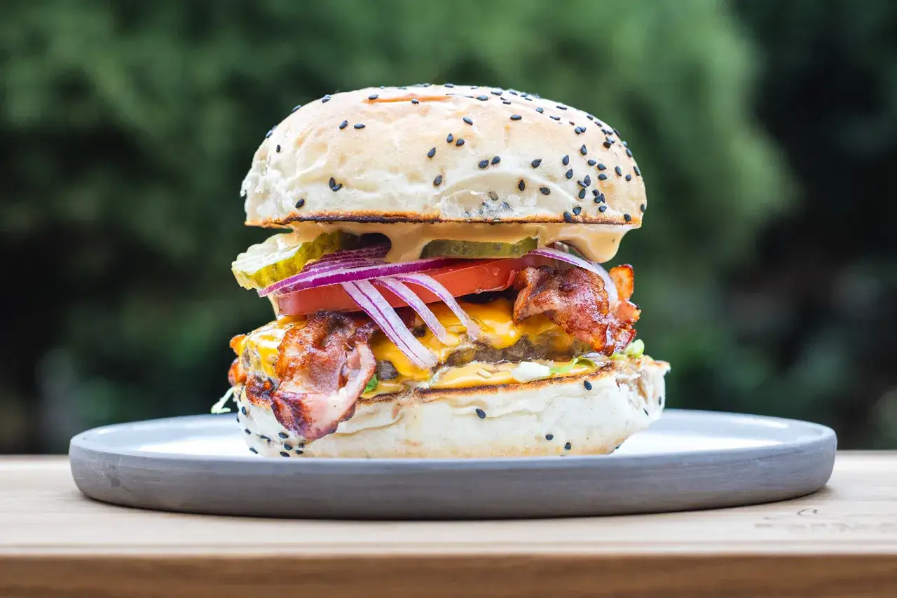 Soczysty burger z bekonem, serem i warzywami na talerzu. Idealny, by pokazać, jak jeść burgera w restauracji.