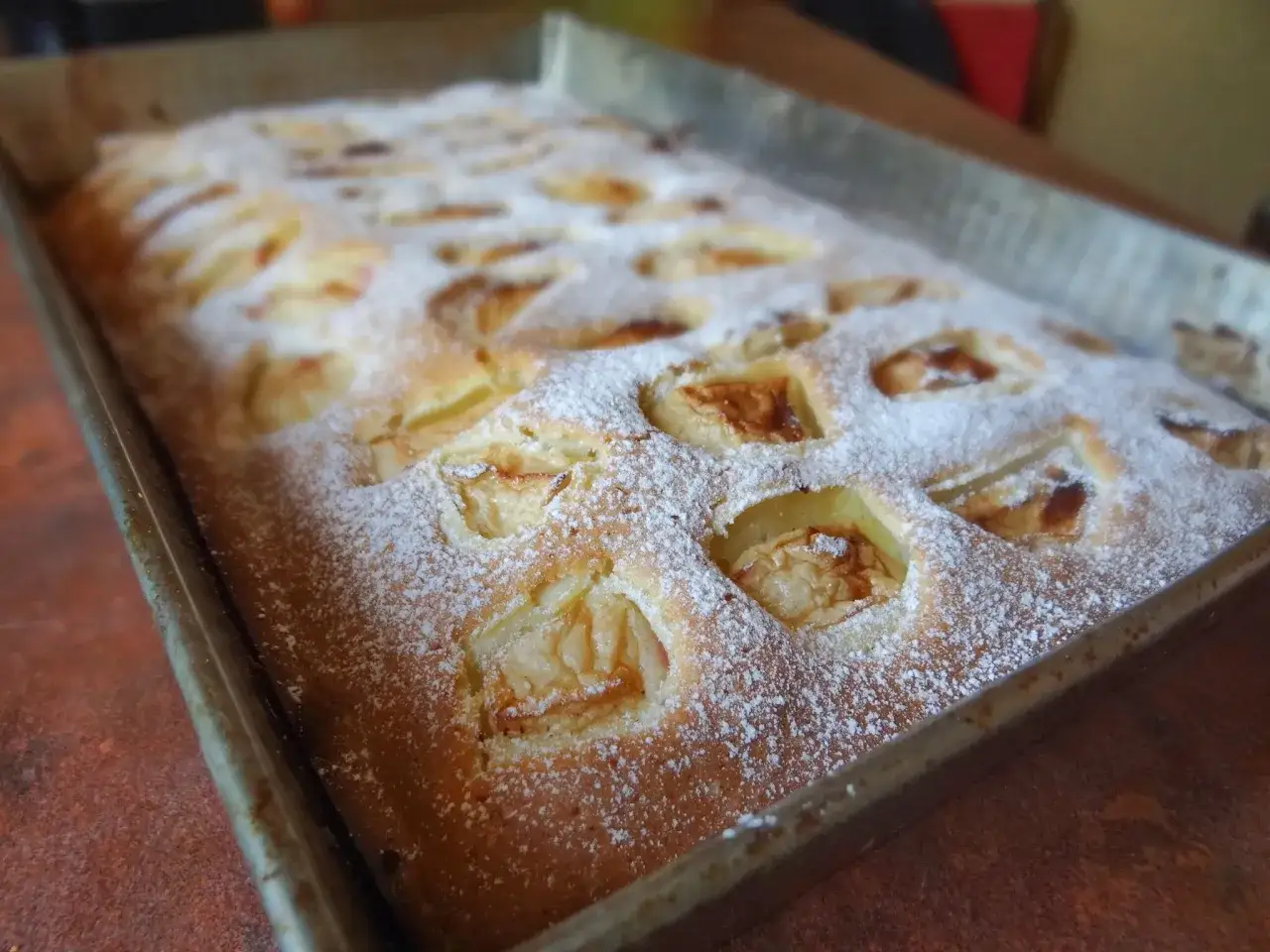 Szybkie i tanie ciasto na dużą blachę z jabłkami, posypane cukrem pudrem. Idealne na rodzinne spotkania.