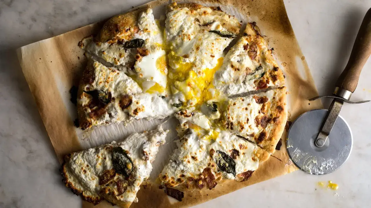 Kawałki pizzy carbonara z płynnym żółtkiem i serem. Obok leży nóż do pizzy.