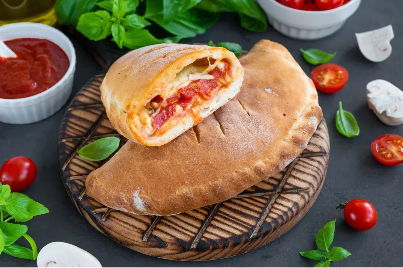 Calzone co to jest? Złocisty, pieczony placek z ciasta drożdżowego, nadziany pomidorami i serem, podany z sosem.