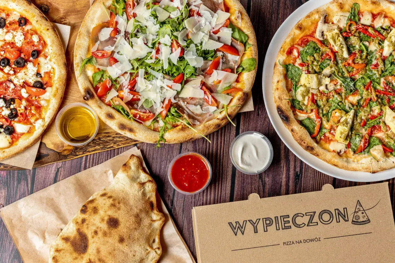 Oto jakie są pizze: jedna z fetą, oliwkami i pomidorami, druga z rukolą, szynką parmeńską i parmezanem, a trzecia z warzywami i pesto. Obok sosy i calzone.