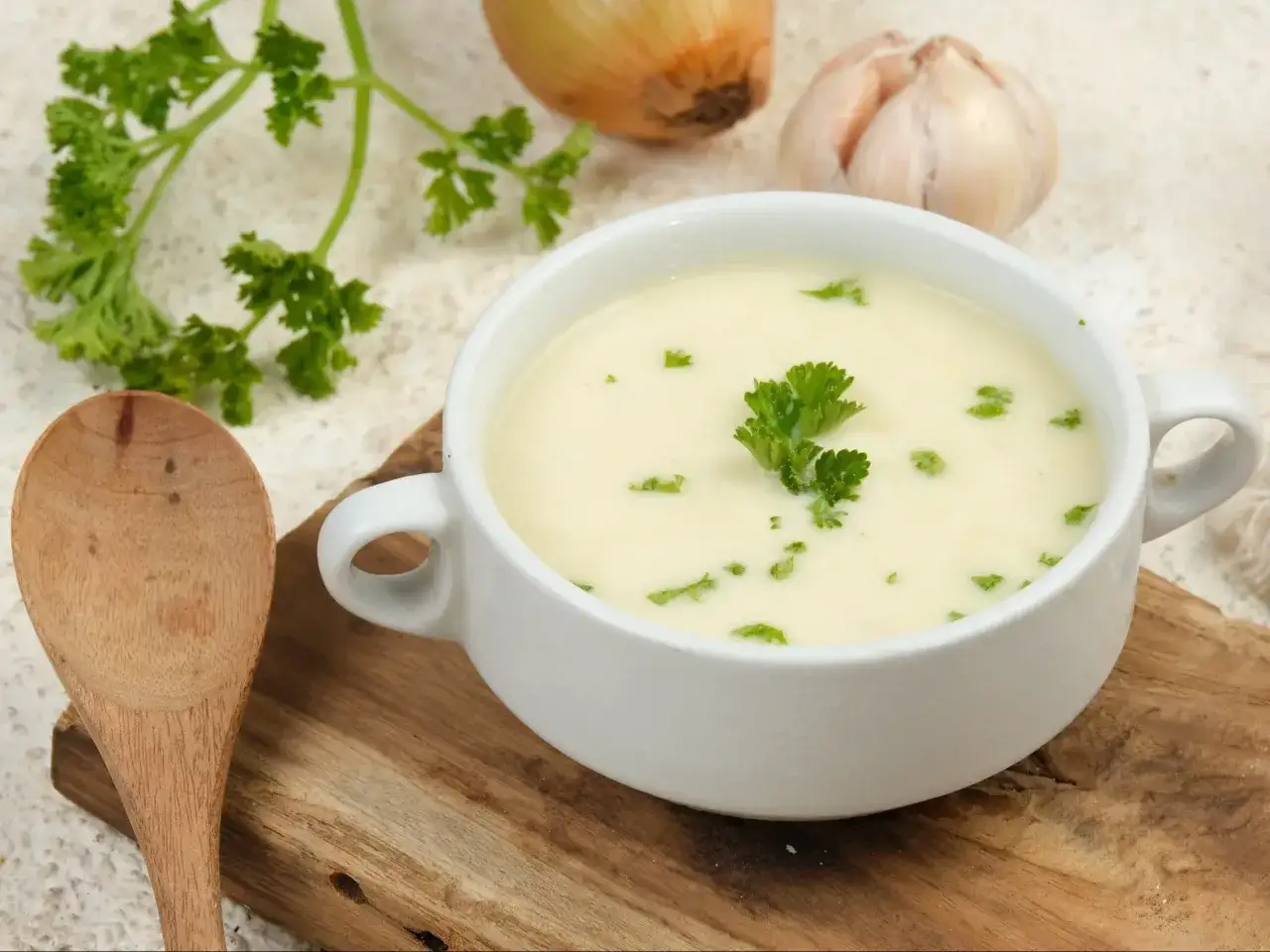 Kremowa zupa lekkostrawna, udekorowana natką pietruszki, obok cebuli i czosnku.