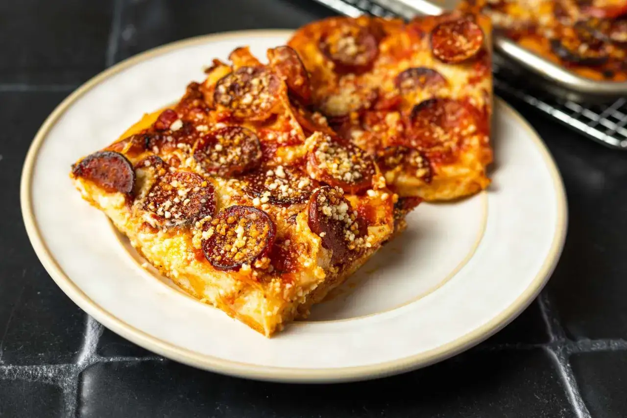 Dwa kawałki pizzy z chrupiącym peperoni i parmezanem na talerzu.