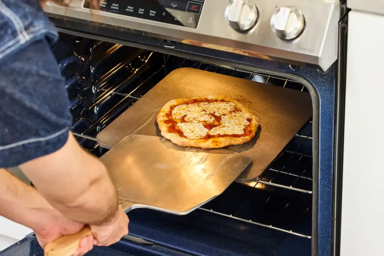 Osoba wkłada do pieca pizzę na kamieniu. Idealnie, ile piec pizze, tyle radości!