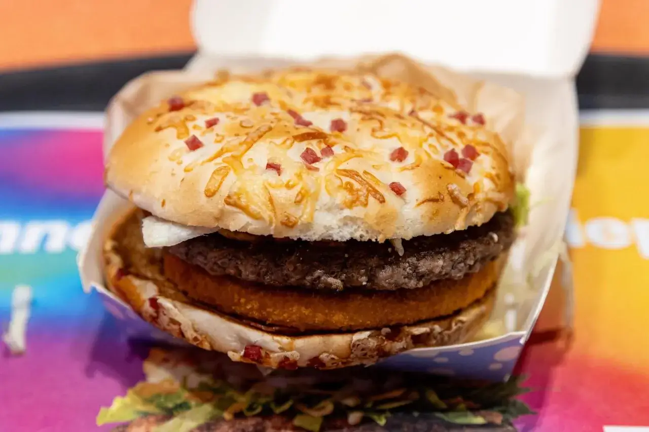 Apetyczny burger drwala z podwójnym mięsem, chrupiącym plackiem ziemniaczanym i bułką posypaną serem i kawałkami boczku.
