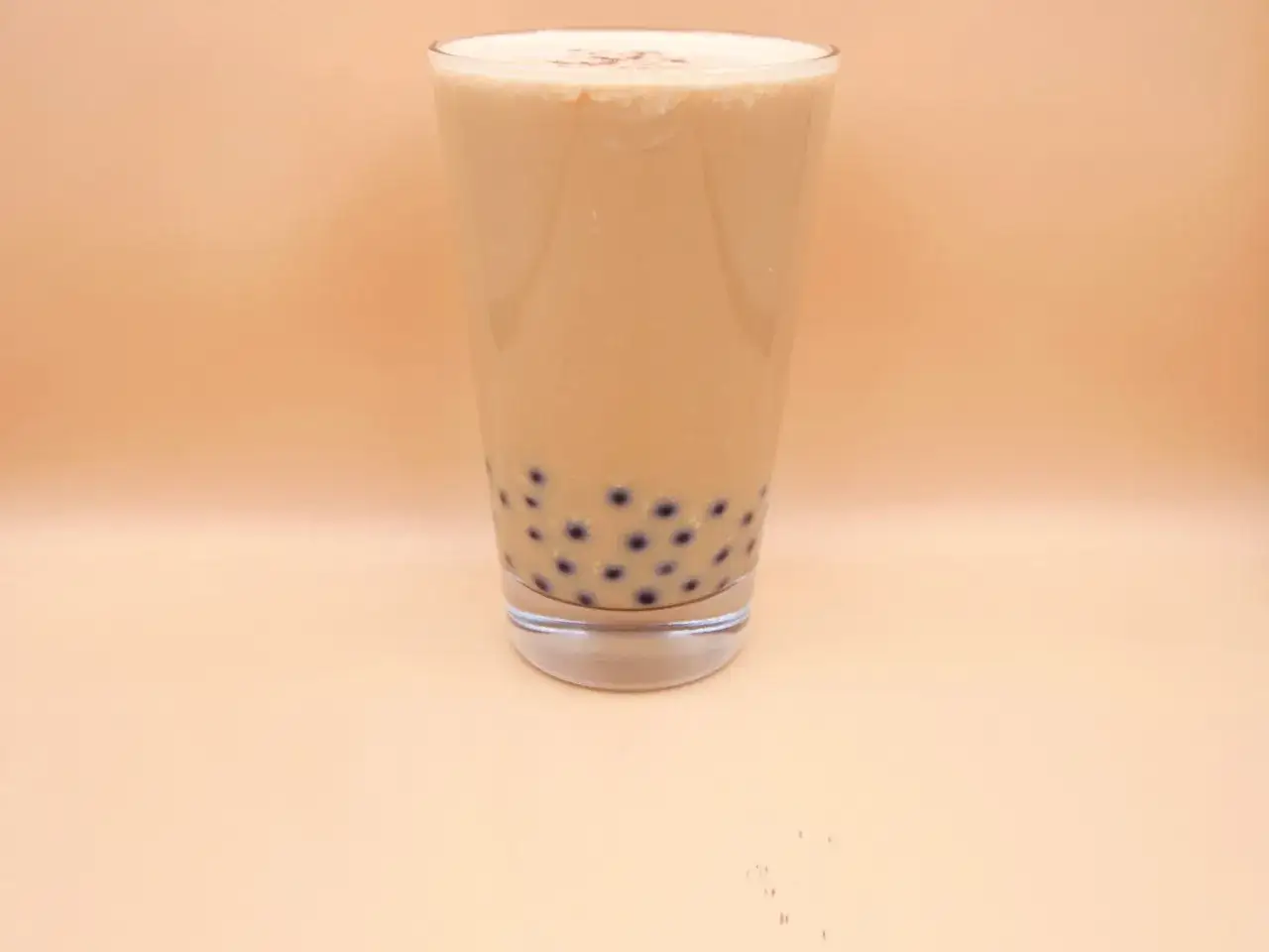 Szklanka z mlecznym napojem i ciemnymi kuleczkami na dnie. Idealny przepis na to, jak zrobić bubble tea.