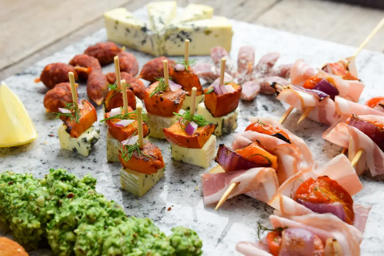 Pyszne przekąski na grilla: szaszłyki z boczkiem i warzywami, mini kiełbaski, ser pleśniowy z dynią i pesto.