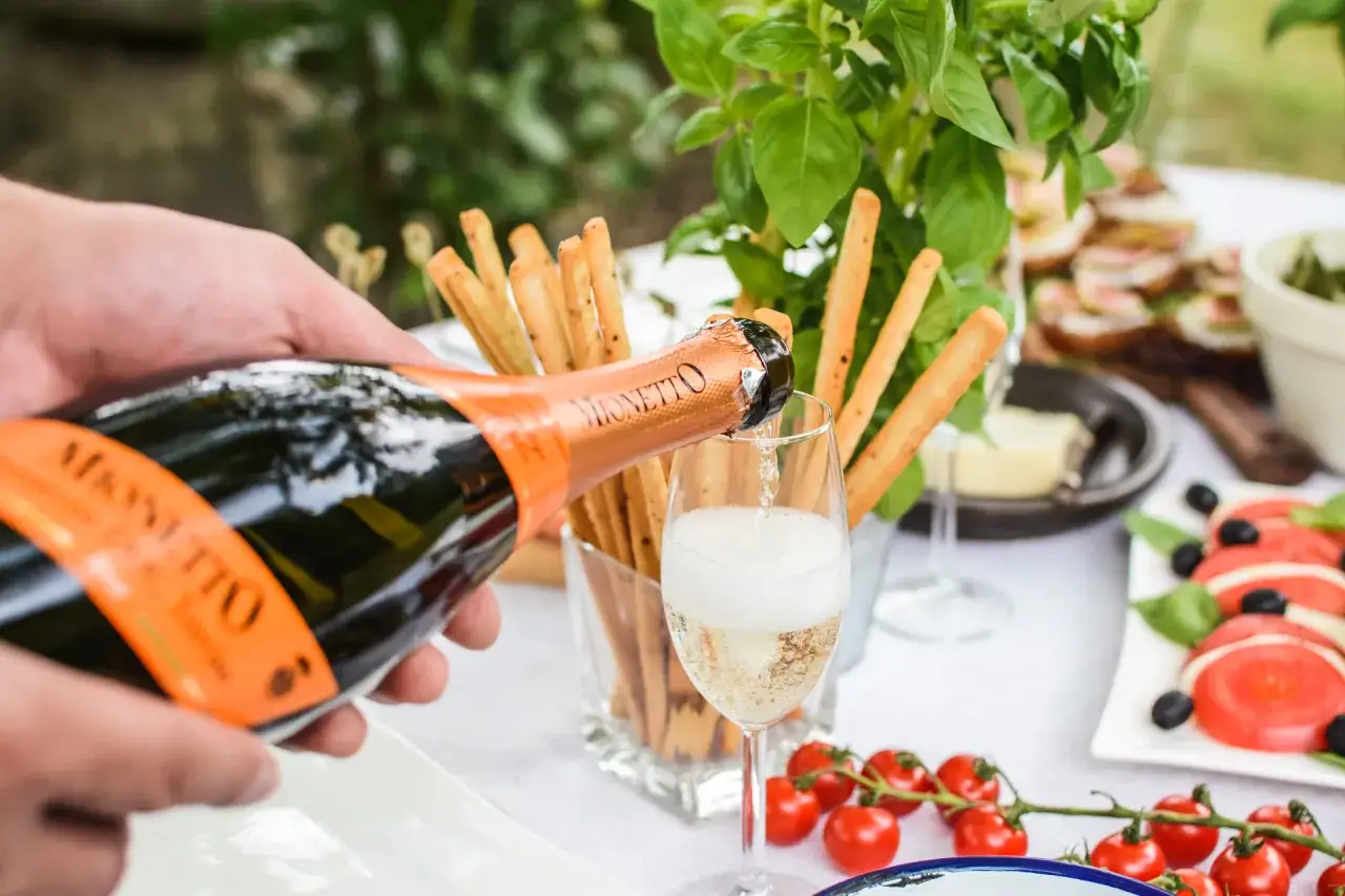 Nalewanie prosecco do kieliszka, obok grissini i pomidorków. Idealny początek włoskiego wieczoru, menu pełne smaków.