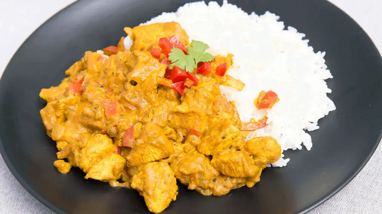 Kurczak w aromatycznym sosie curry z ryżem, ozdobiony papryką i kolendrą. Pyszne danie gotowe do podania.