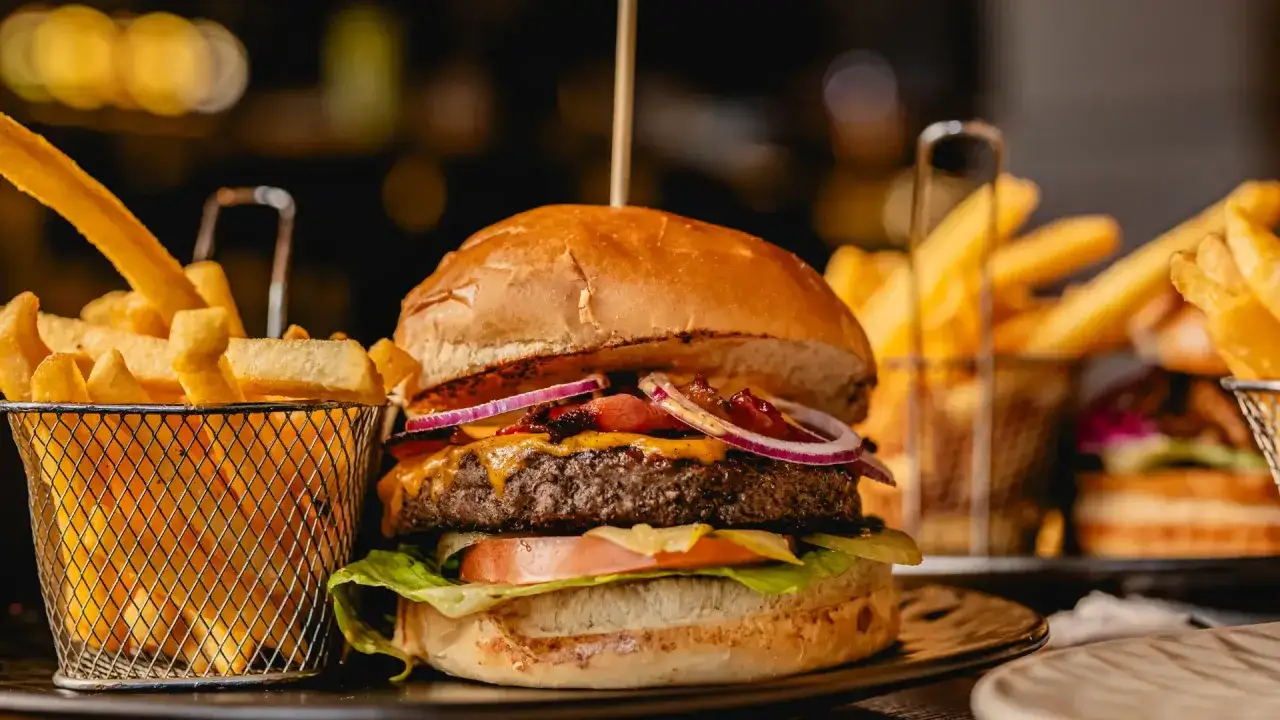 Soczysty burger z bekonem, serem i czerwoną cebulą, podany z chrupiącymi frytkami. Idealny zestaw, co do burgera!