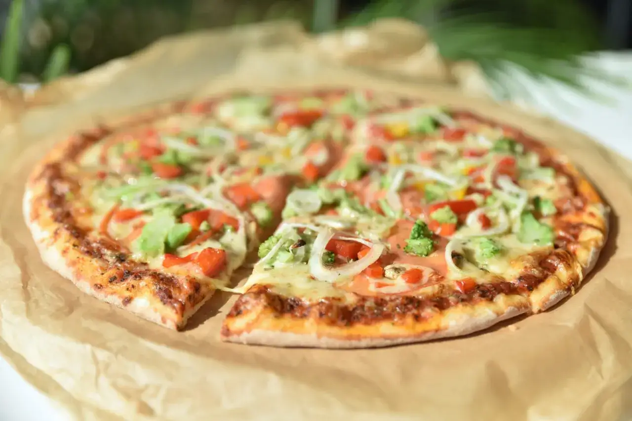 Pyszna pizza bez mięsa z brokułami, papryką i cebulą, podana na papierze do pieczenia.