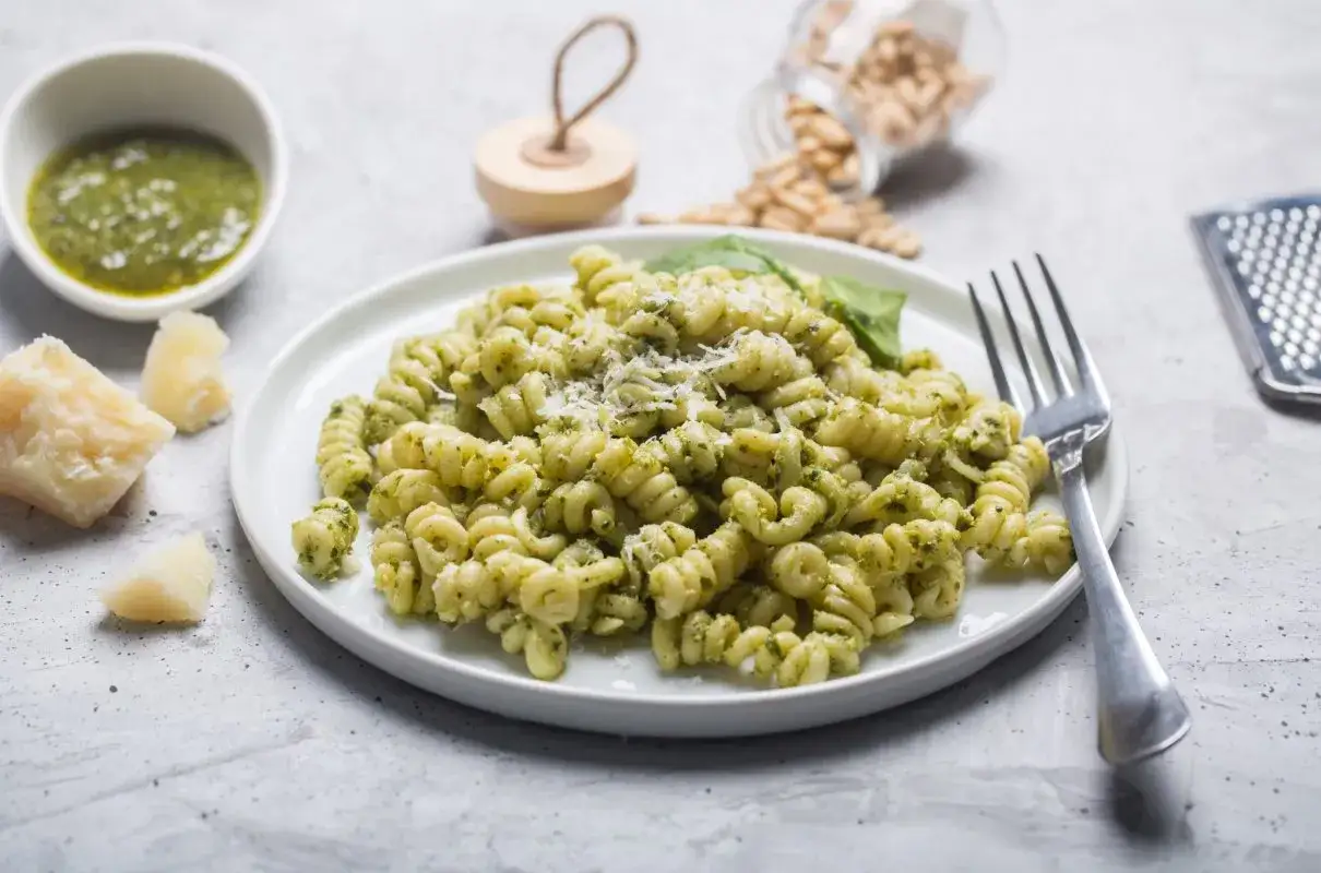 Fusilli z aromatycznym makaronem z pesto ze słoika, posypane parmezanem. Obok kawałki sera i pini.