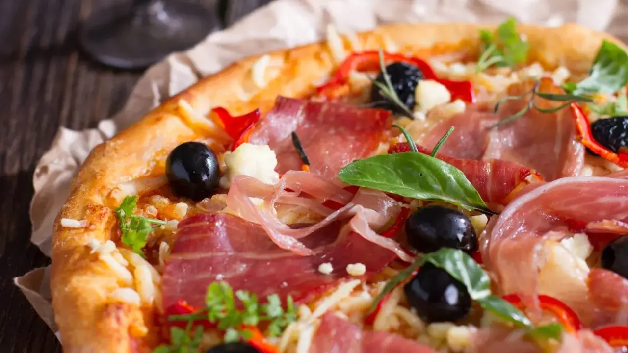 Pyszna pizza z cienko pokrojoną, aromatyczną szynką, czarnymi oliwkami i papryką. Idealna na każdą okazję, zastanawiasz się jaka szynka na pizzę będzie najlepsza?