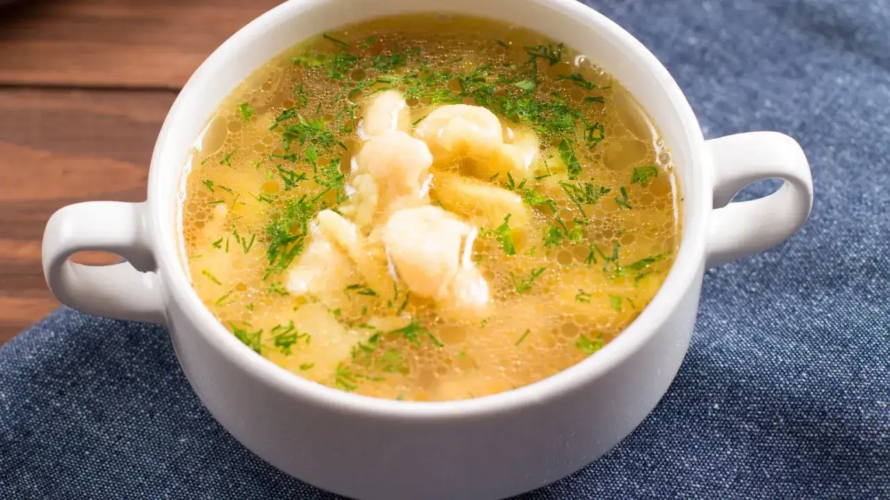 Aromaticzna zupa zacierkowa z koperkiem w białej miseczce, podana na granatowym obrusie.