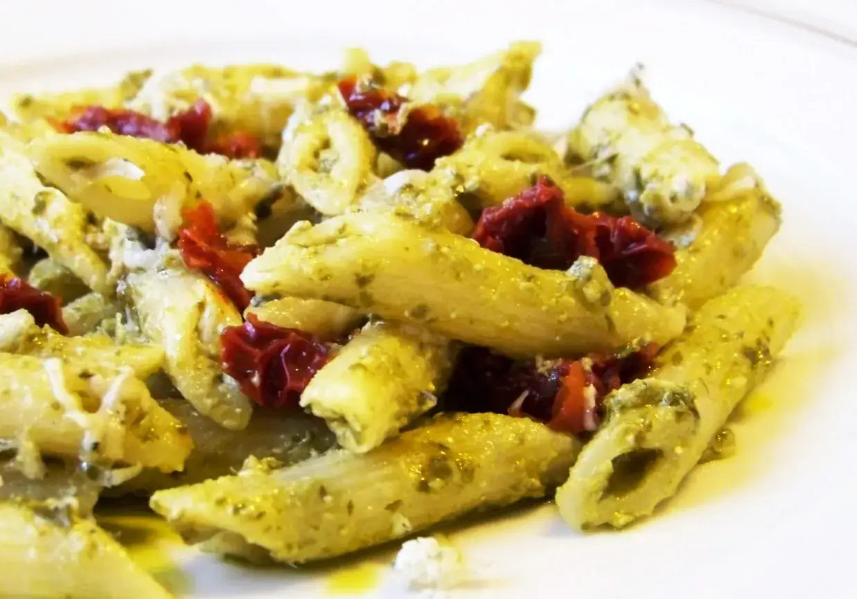 Penne z aromatycznym pesto i słodkimi suszonymi pomidorami, posypane parmezanem. Pyszne danie gotowe do podania.
